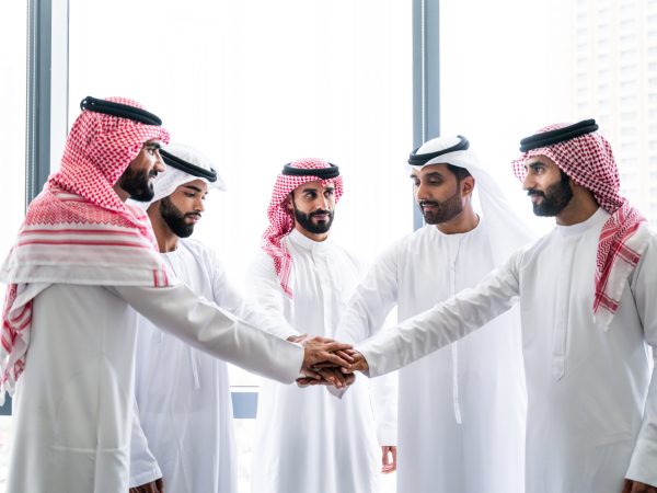 Arab businessmen wearing emirati and saudi kandura meeting in office for business deal - Corporate business group of middle-eastern people working in an international company in middle east